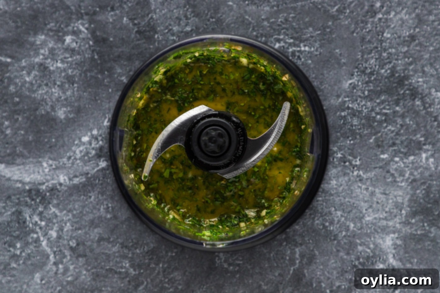 Blitzed chimichurri ingredients in a mini food chopper, showing coarse texture