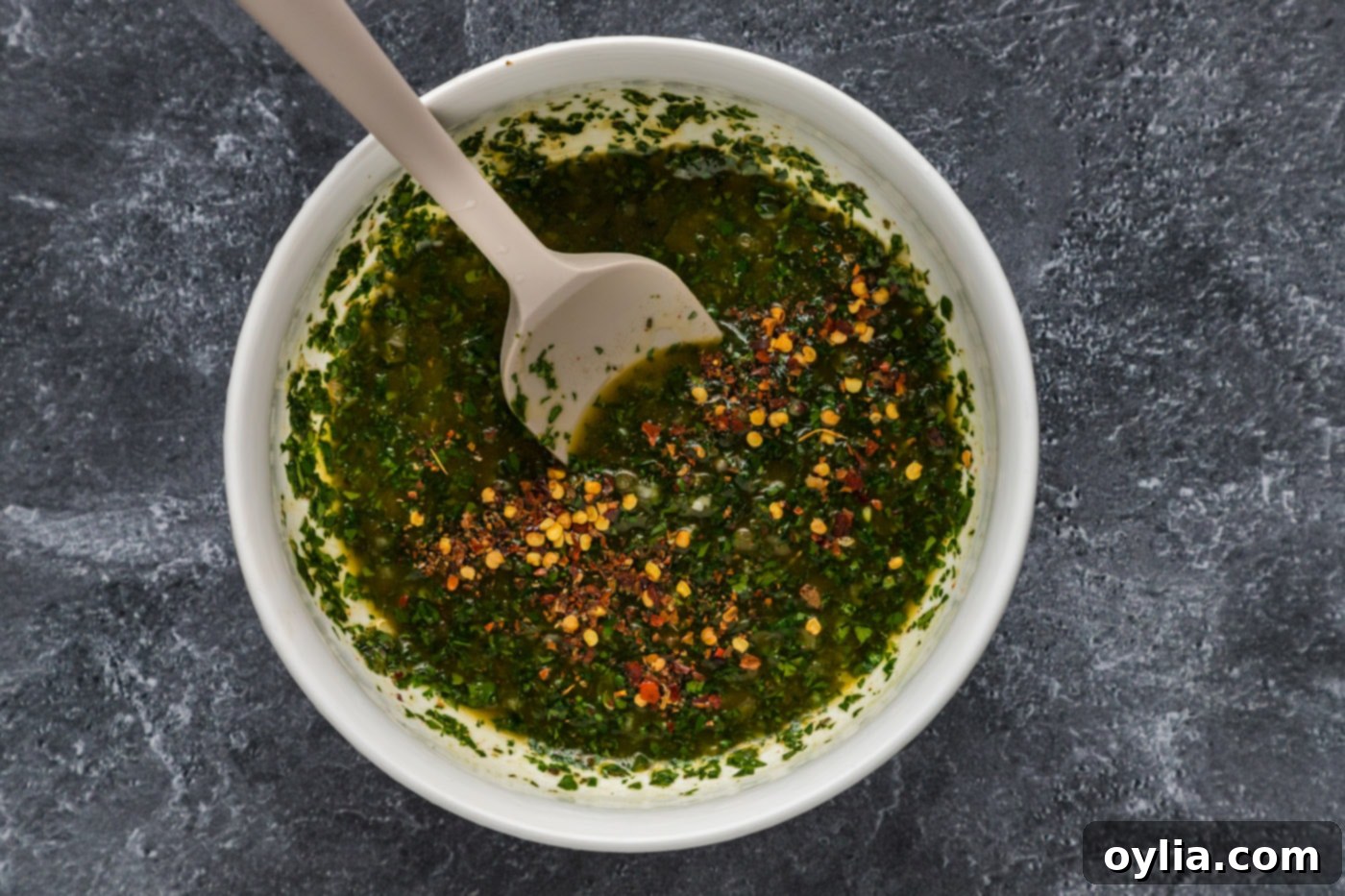 Chimichurri sauce in a mixing bowl with red pepper flakes stirred in