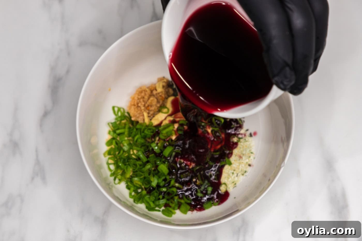 pouring red wine over garlic, rosemary, chili powder, mustard powder, Dijon mustard, and green onion