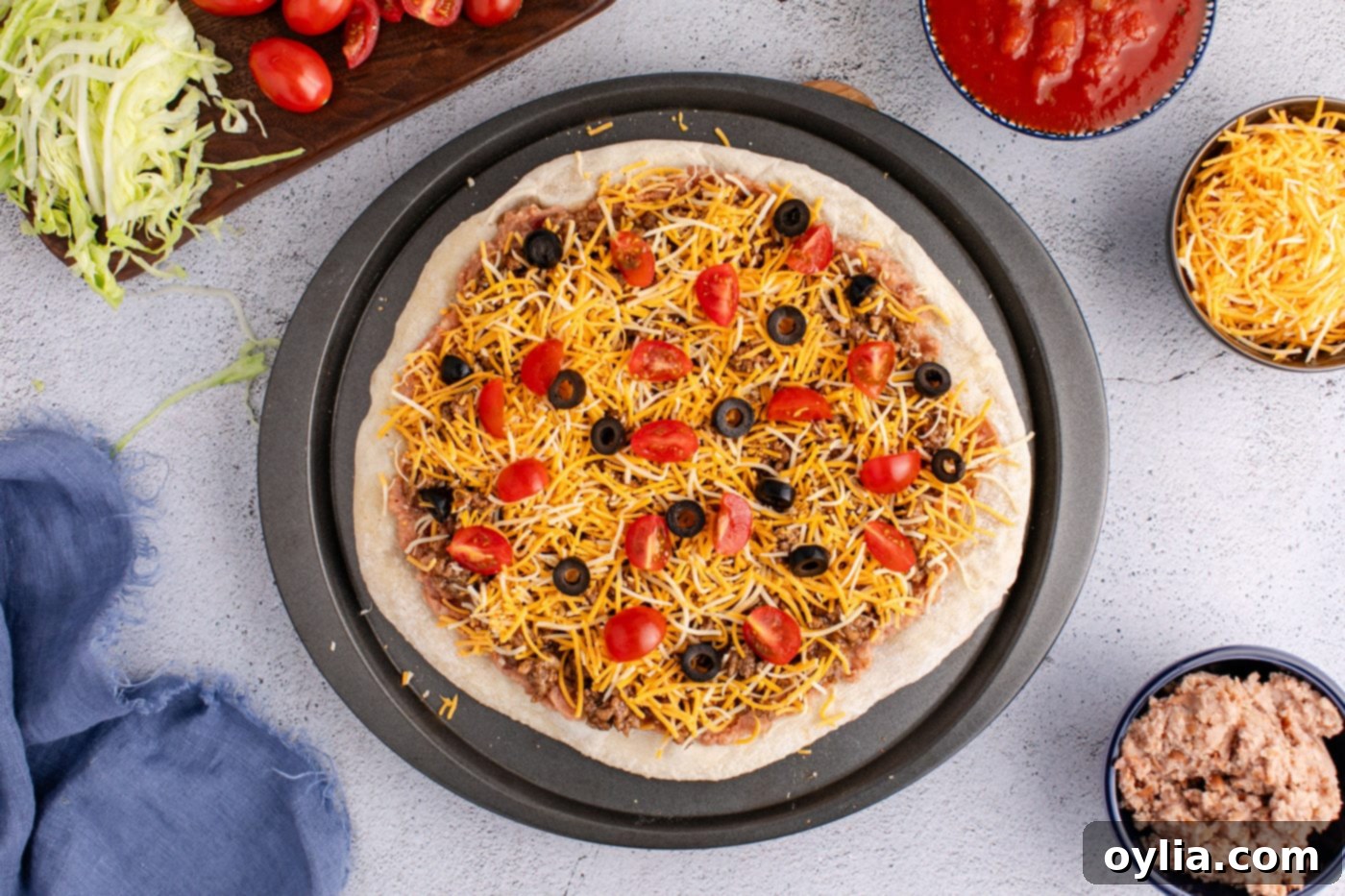 shredded cheese, taco meat, tomatoes, and olives added on top of refried beans and pizza crust
