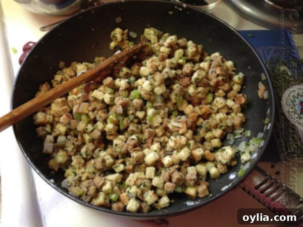 A close-up photo of cubed stuffing with chopped onions and celery being tossed in a skillet.