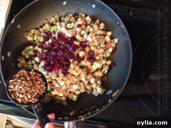 A photo showing dried cranberries and pecans being added to the stuffing mixture in the skillet.