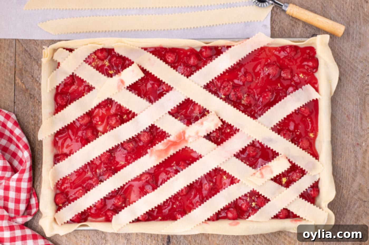 Arranging the pie crust weave on top of the cherry pie filling, showing the intricate pattern of the lattice crust taking shape.