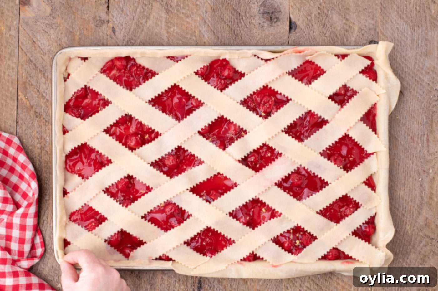 The edges of the cherry slab pie crust are being pinched together to form a sealed border around the lattice top, securing the filling.