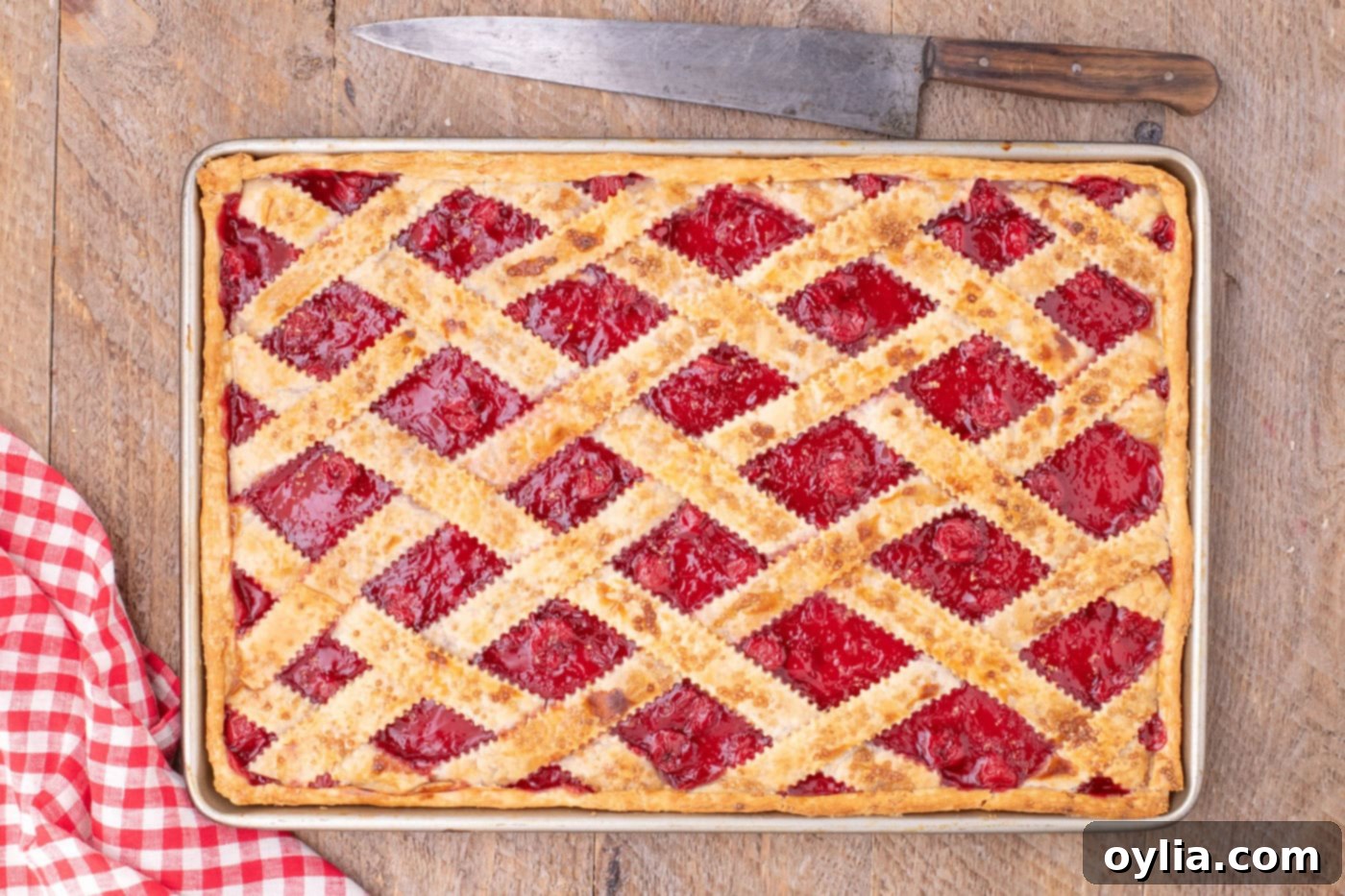 An overhead view of a beautifully baked cherry slab pie in a jelly roll pan, with a perfectly golden lattice crust and bubbling filling, cooling on a rack.