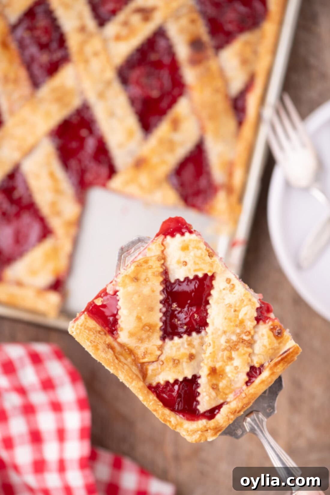 A spatula lifting a perfect square slice of golden Cherry Slab Pie, revealing the rich cherry filling, with the rest of the pie in the background.