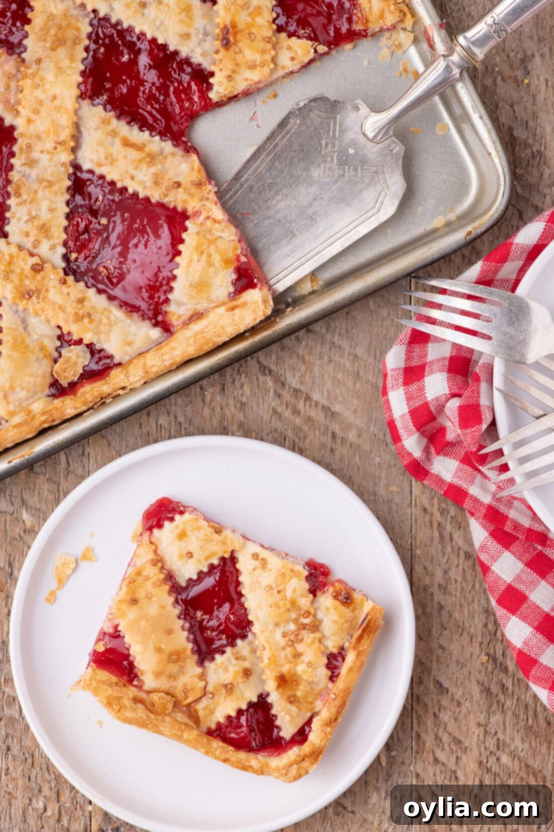 A perfect slice of Cherry Slab Pie on a white plate, with the large slab pie visible in the background, showcasing its golden crust and juicy filling.