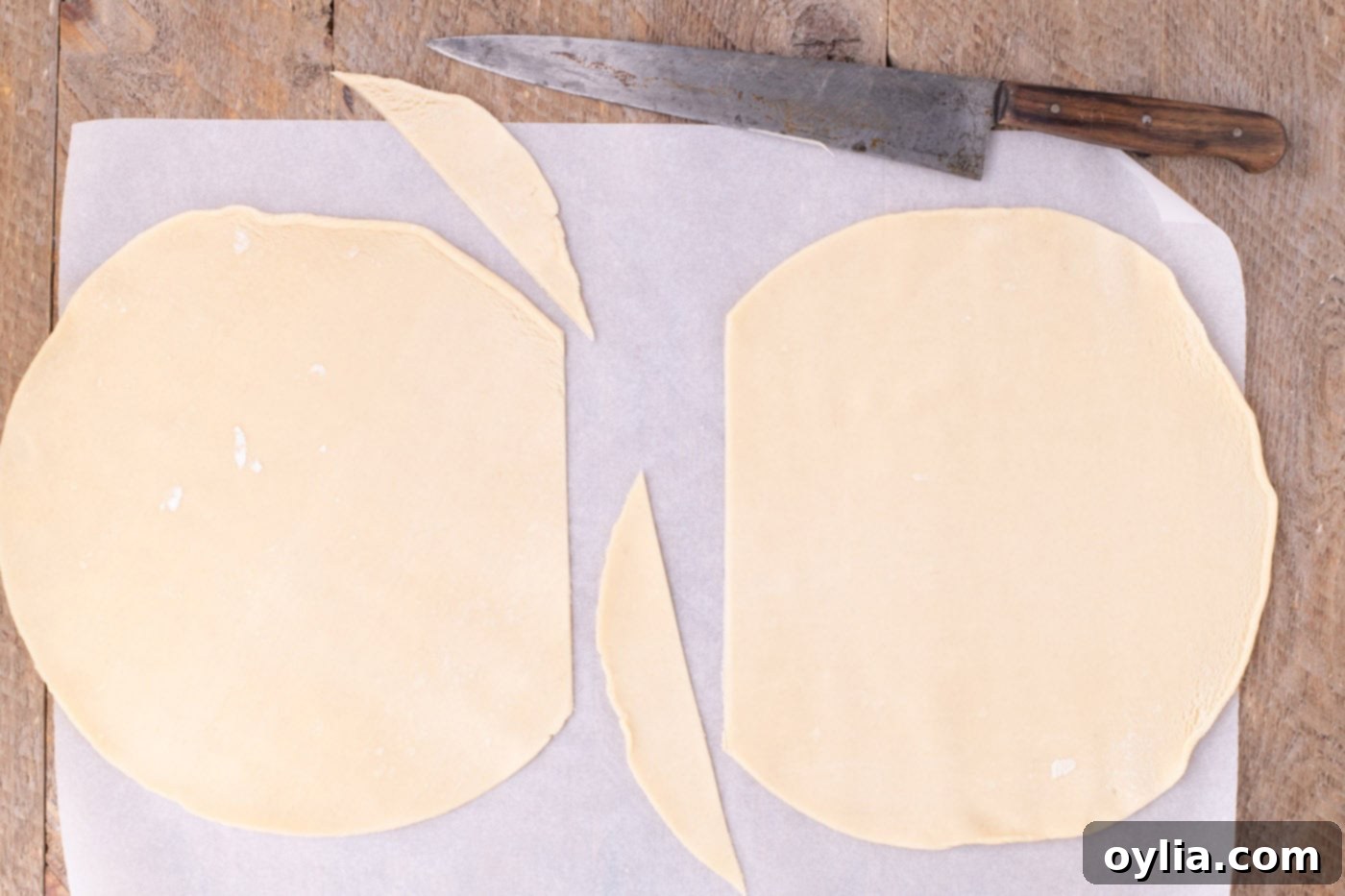 Two trimmed premade pie crusts laid side by side on parchment paper, ready for merging to form the base of the slab pie.