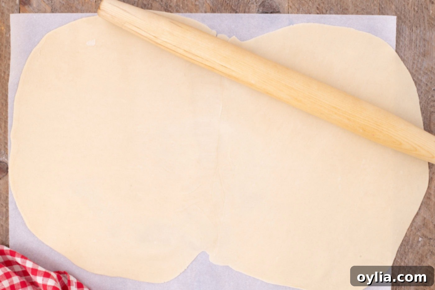 A rolling pin being used to seamlessly join and flatten two pre-made pie crusts into one larger rectangular sheet for the slab pie base.