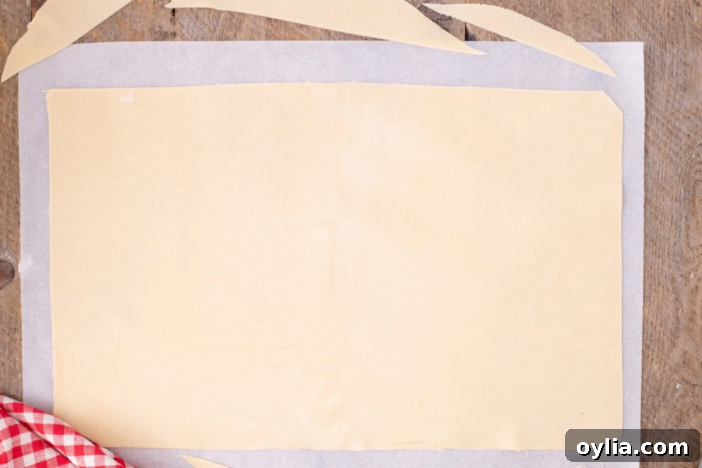 A neatly trimmed rectangular pie crust laid out on parchment paper, perfectly sized to fit a jelly roll pan with an overhang.