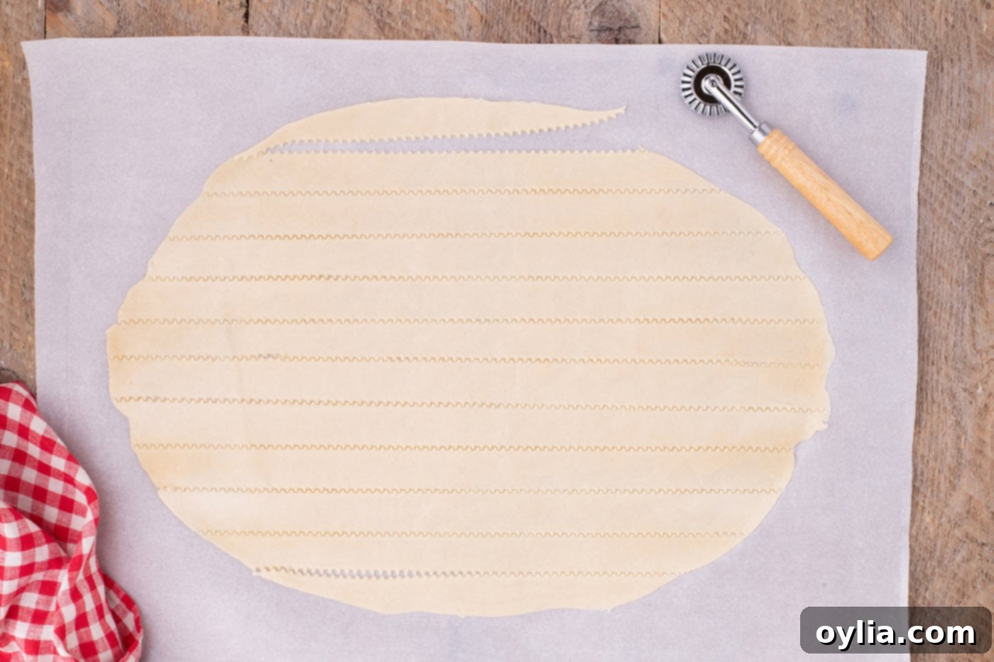 A pastry cutter and ruler being used to precisely slice a rolled-out pie crust into even 1-inch wide strips for a lattice top.