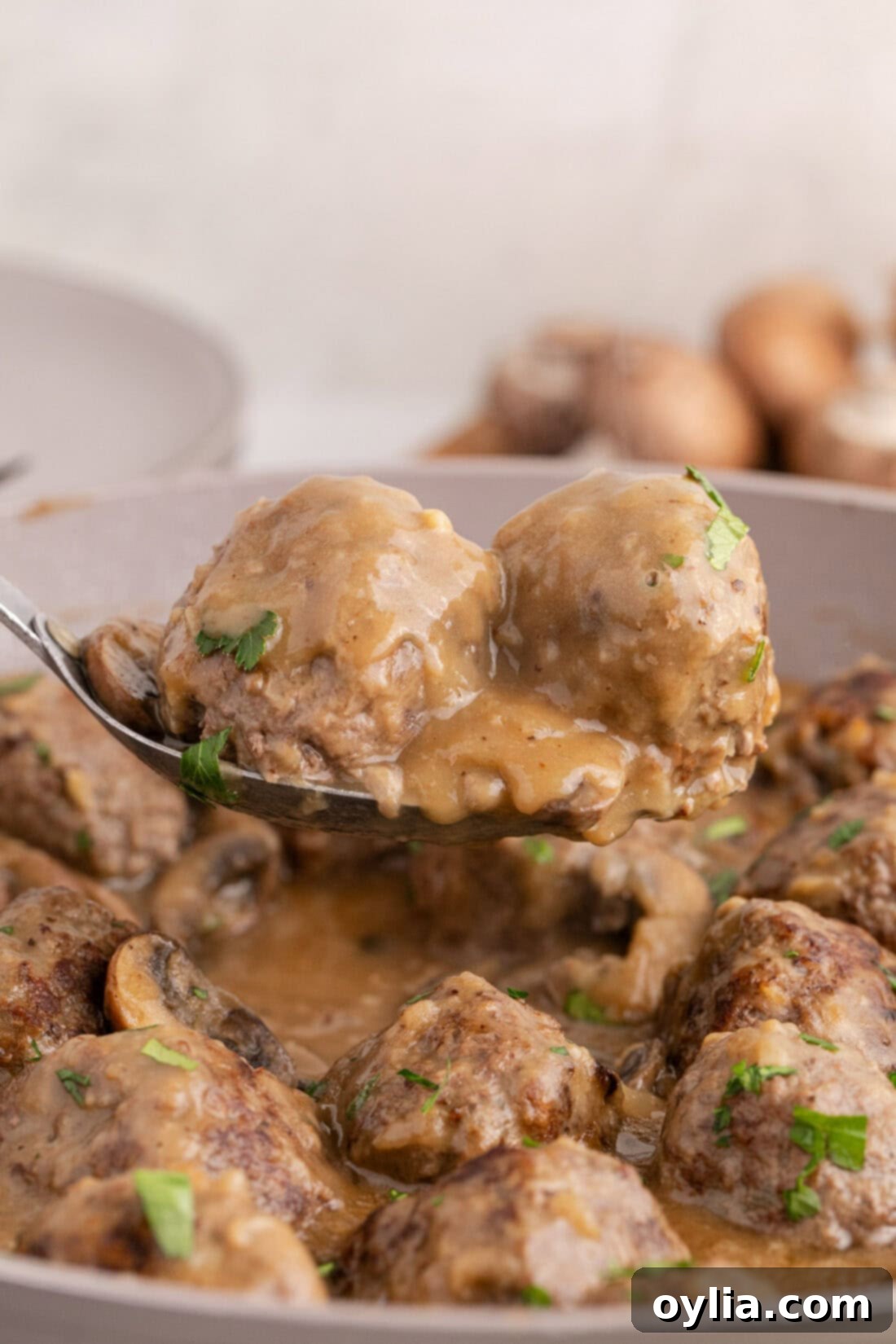 Two Salisbury Steak Meatballs on a spoon held above a skillet of Salisbury Steak Meatballs, ready to be served