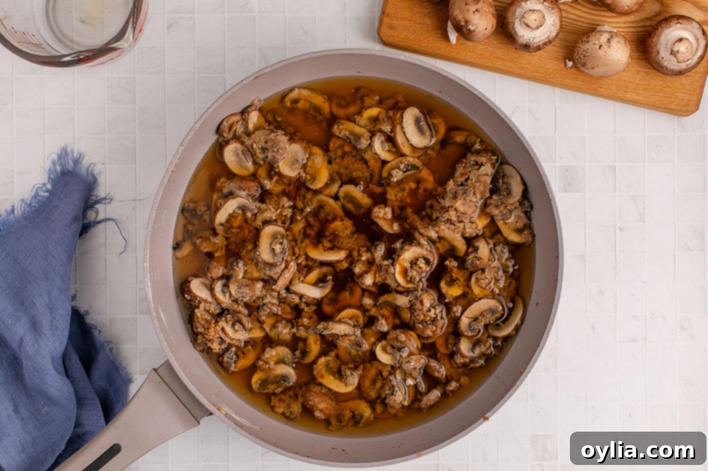 Beef broth and Worcestershire sauce being added to the mushroom sauce, whisking to prevent lumps
