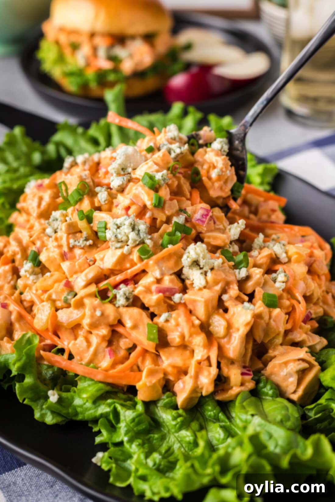 Buffalo Chicken Salad 2 Buffalo Chicken Salad on a bed of lettuce with a spoon in it, showcasing its creamy texture and vibrant colors.