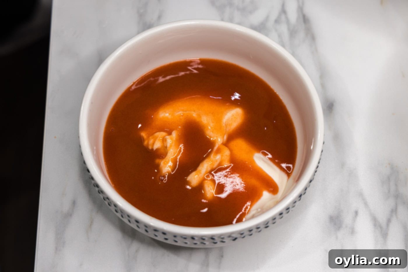 Hot sauce and mayonnaise are whisked together in a small bowl to create the buffalo dressing.