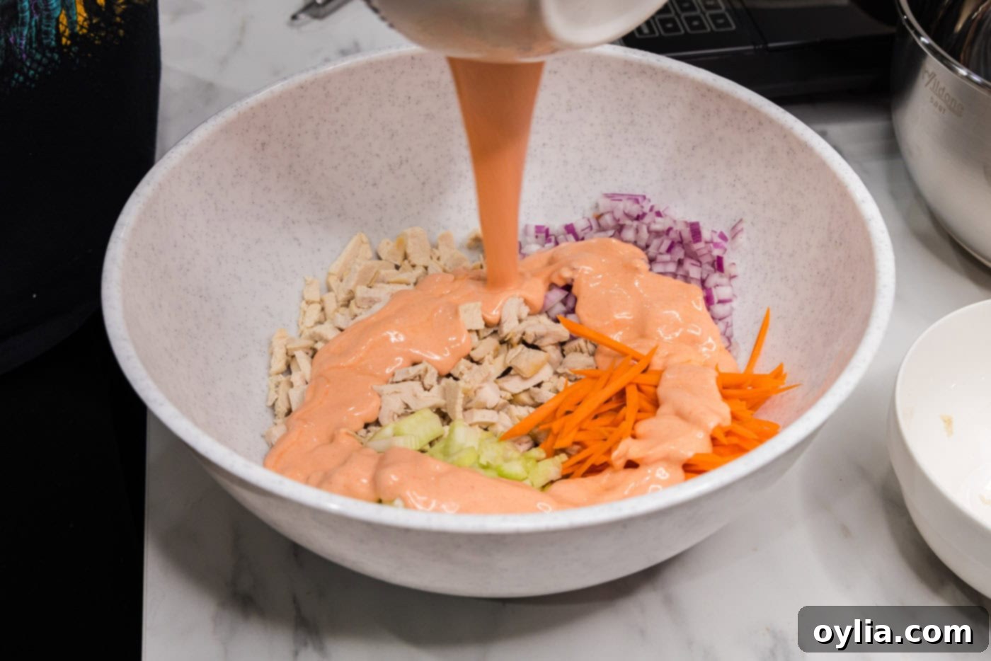 Buffalo sauce being poured over the mixture of chicken and vegetables in a bowl.