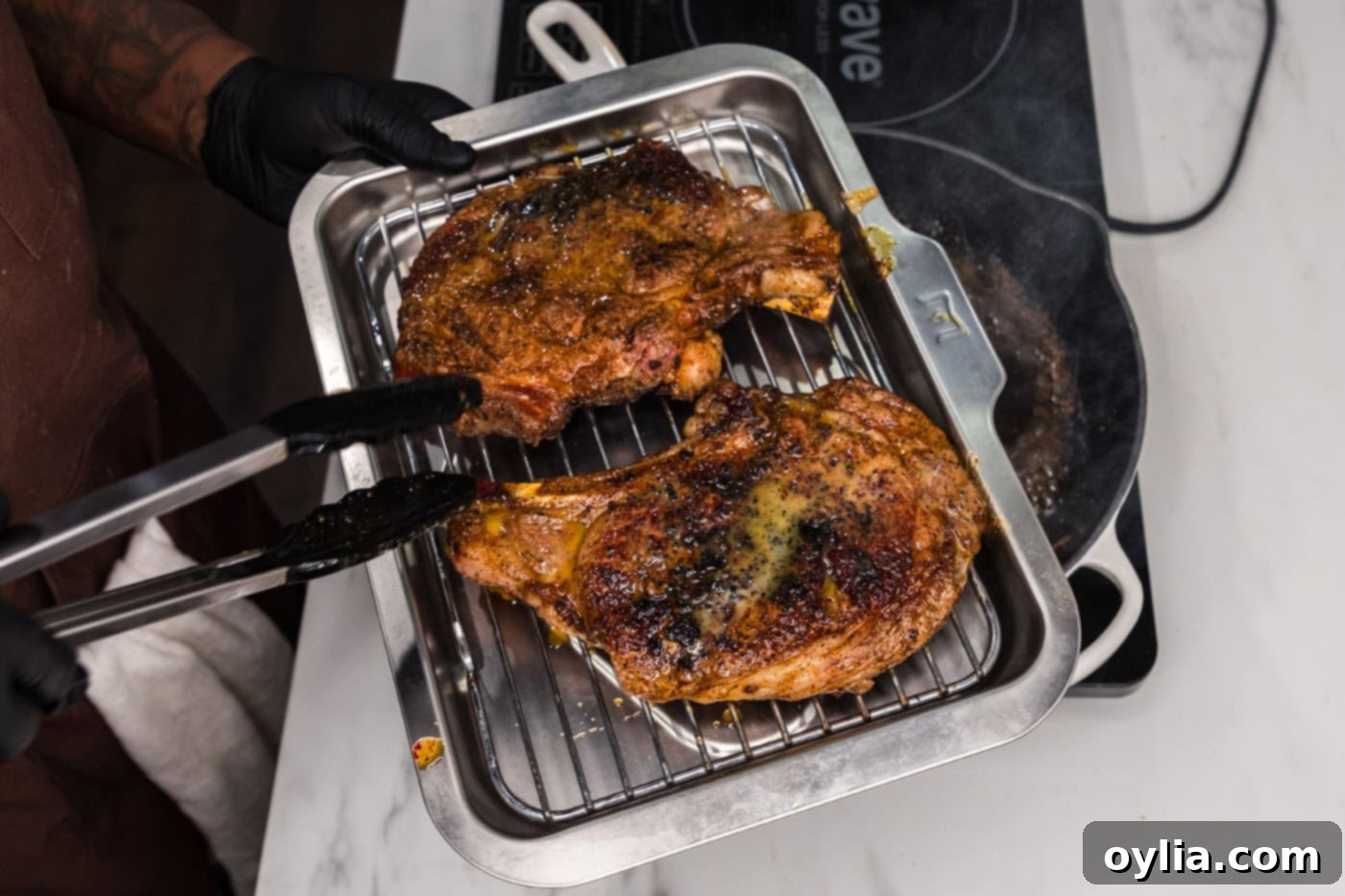 Transferring a skillet with seared ribeye steaks into the oven for the final cooking phase.