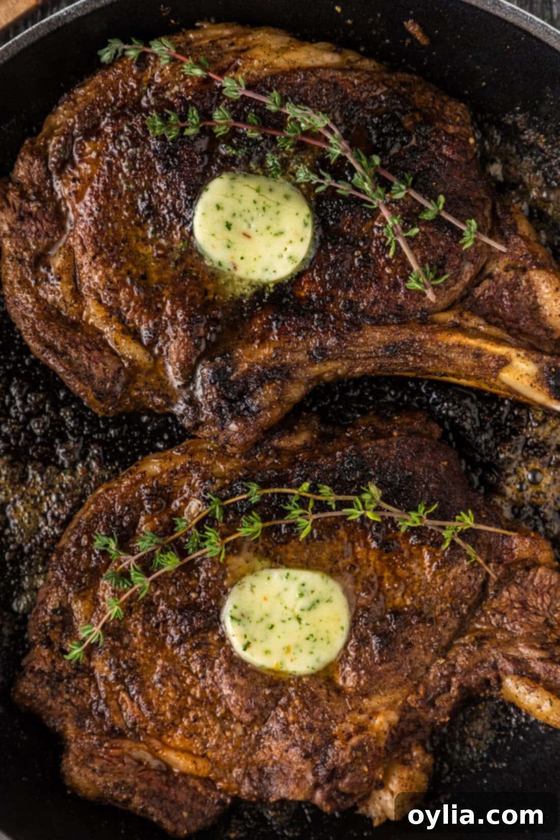 Close up photo of two sizzling bone-in ribeye steaks developing a perfect crust in a hot skillet.