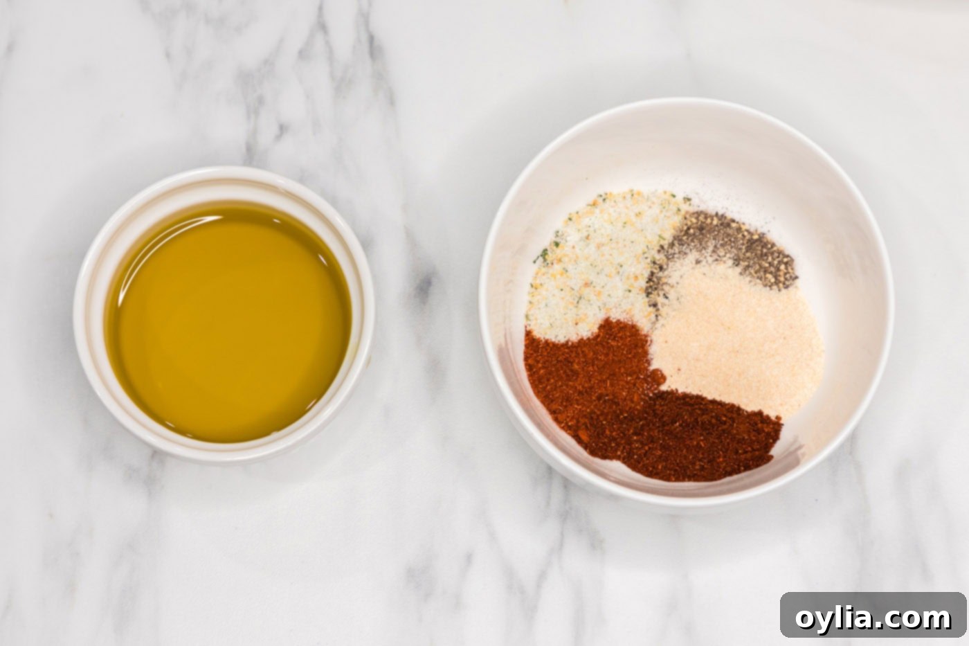Olive oil in a small bowl next to a blend of various seasonings, ready to be mixed for the steak rub.