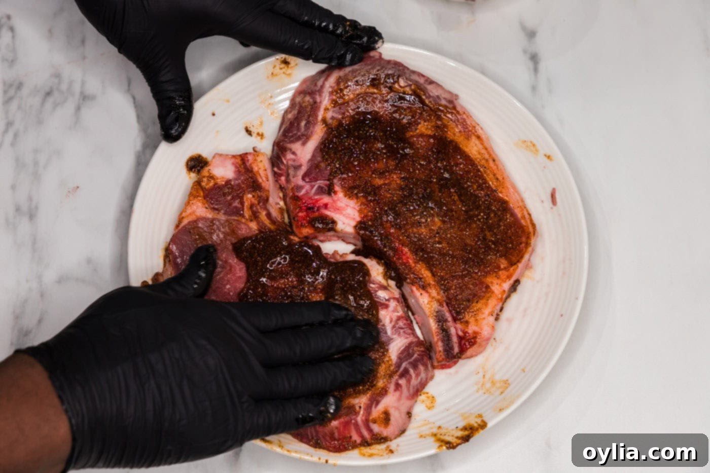 Hands meticulously rubbing a wet spice mixture onto a bone-in ribeye steak.