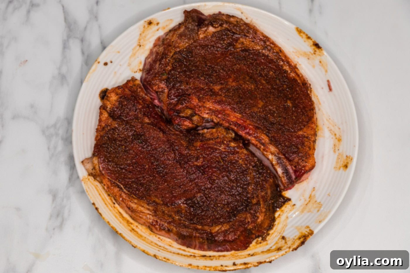 Two bone-in ribeye steaks beautifully seasoned and resting on a plate, ready for searing.