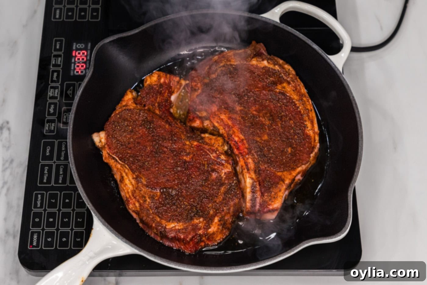 Two thick bone-in ribeye steaks sizzling intensely in a hot cast iron skillet, developing a savory crust.