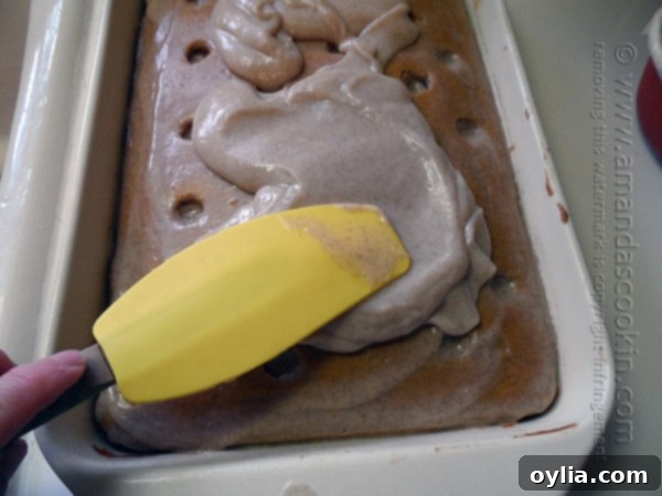 A close up photo of pudding being spread over the pumpkin cake with a spatula. 