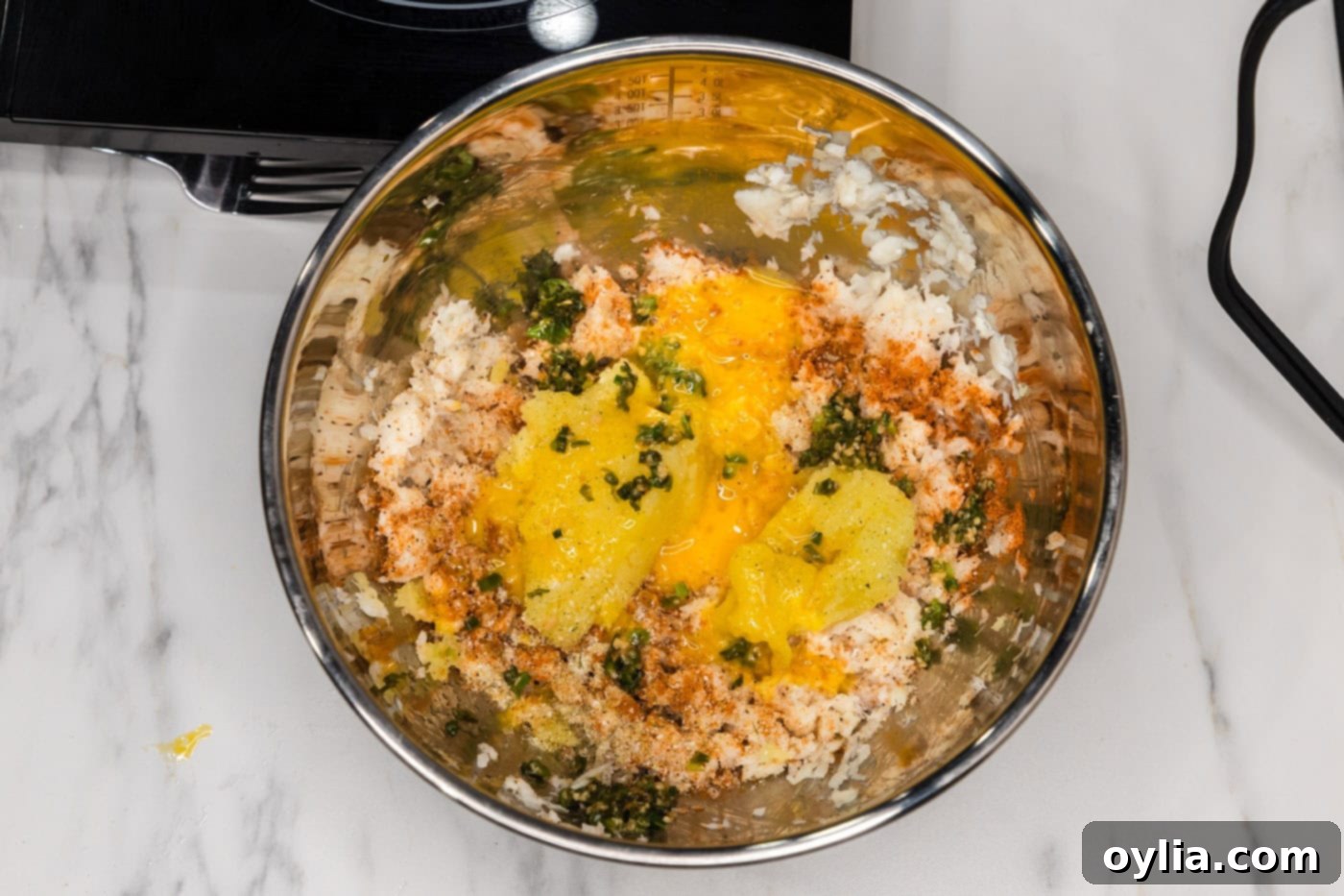 flaked fish with seasonings, egg, and mashed potatoes in a bowl, ready to be mixed