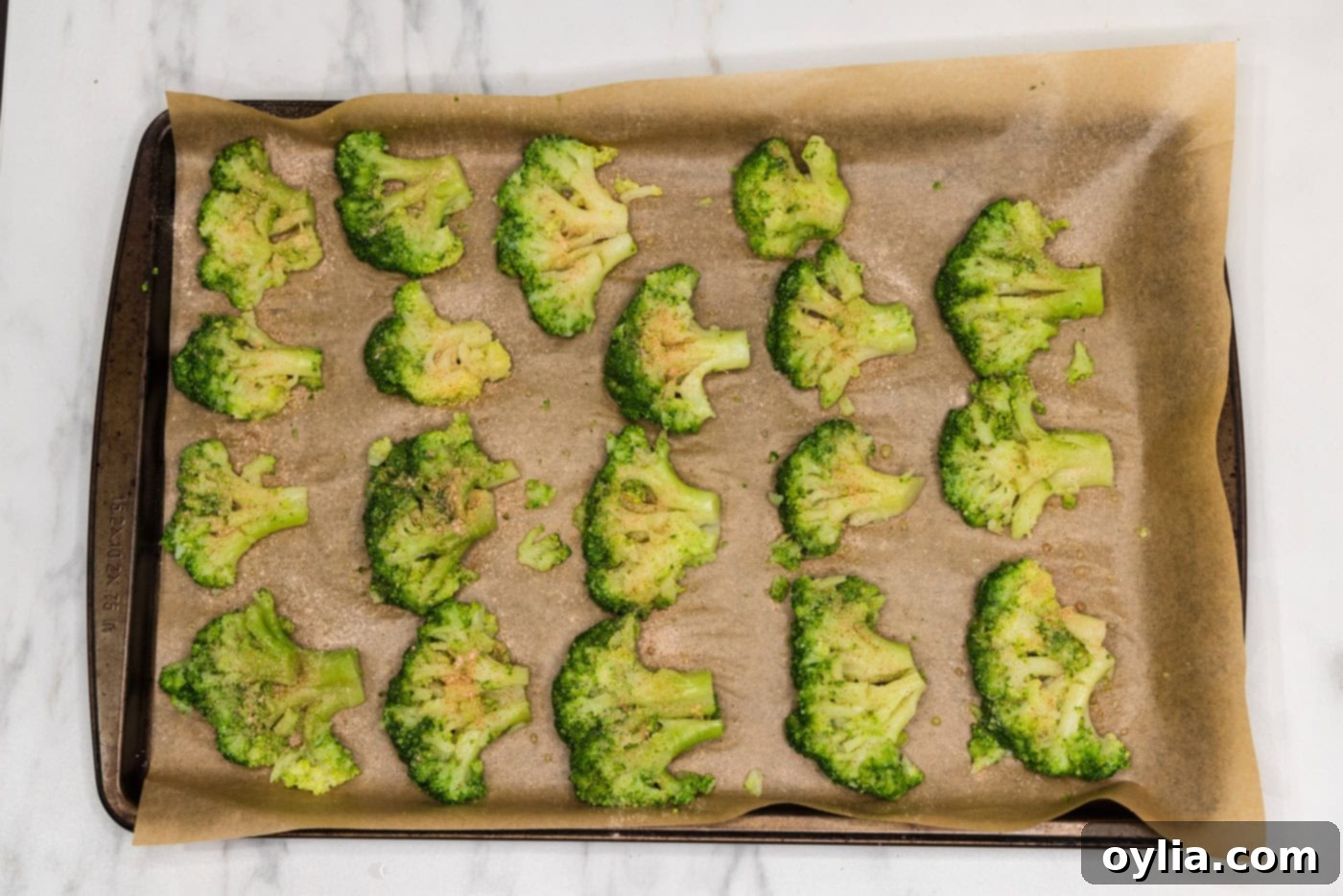 Smashed broccoli florets on a baking sheet, seasoned and ready for parmesan.