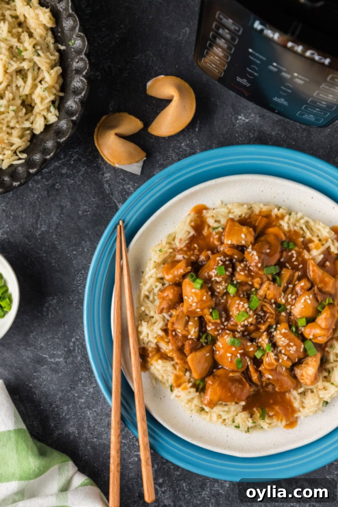 Half a plate of Instant Pot Bourbon Chicken over rice with fortune cookies in the background, showcasing the sticky, glazed chicken.
