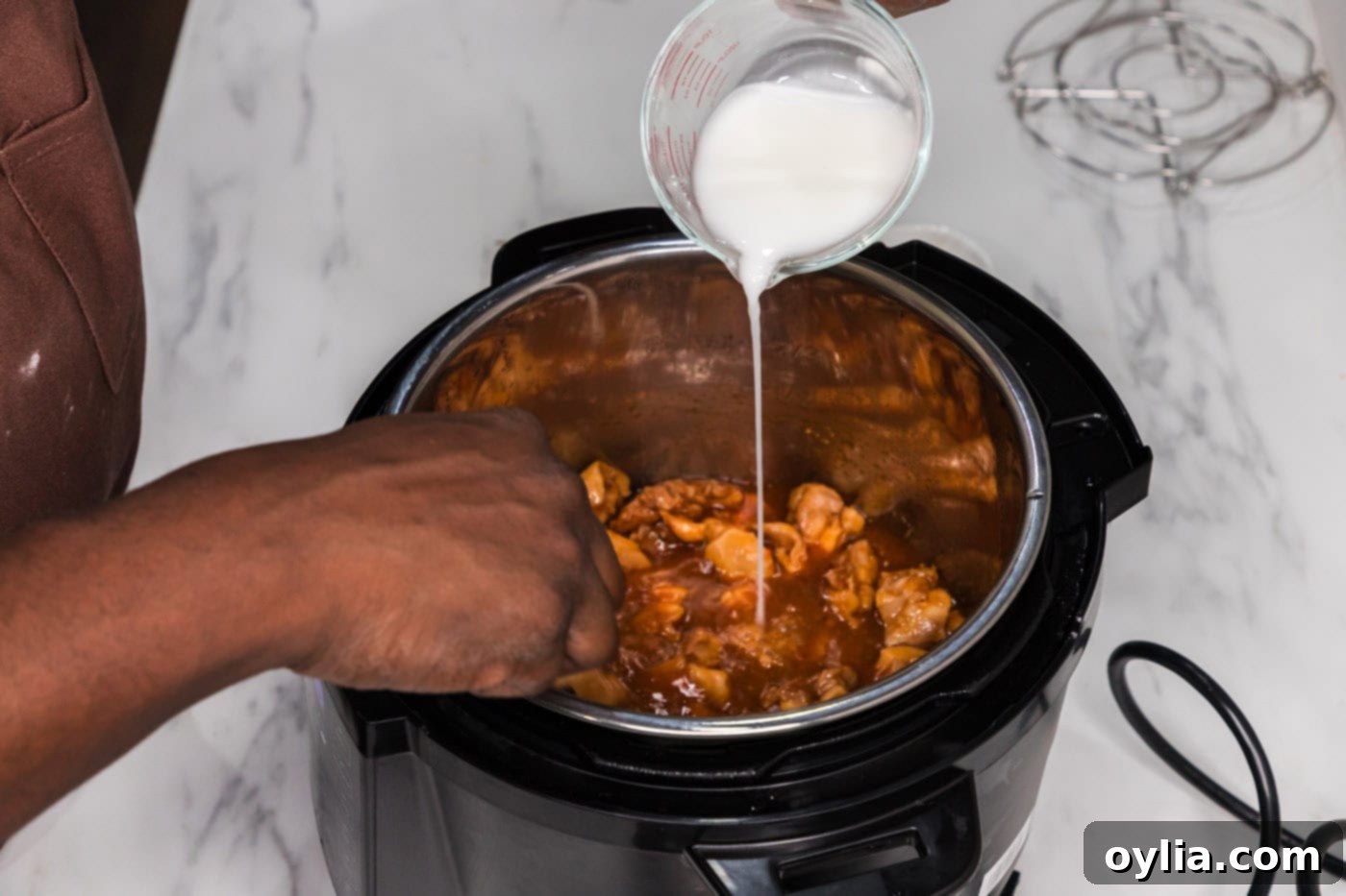 Pouring a cornstarch slurry into the Instant Pot with bourbon chicken, ready to thicken the sauce.