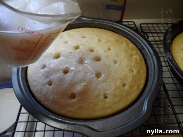 Cream of coconut being poured over a poked cake layer, soaking into the holes.