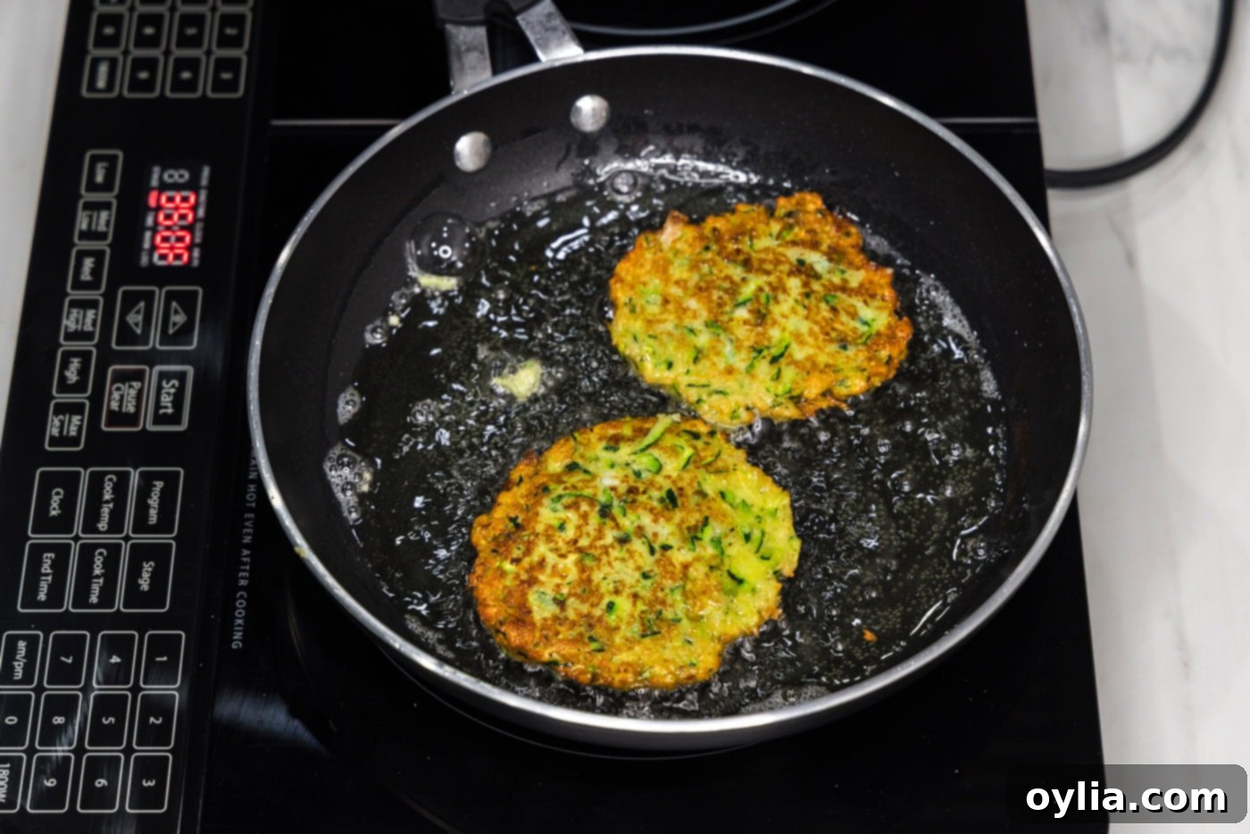 fried zucchini fritters in a skillet of oil