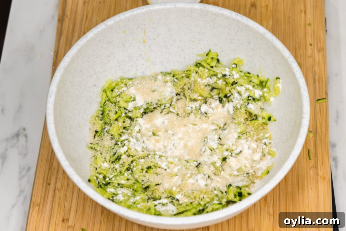 flour and breadcrumbs added to shredded zucchini mixture in a bowl