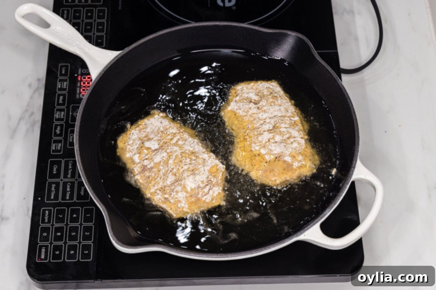 Frying golden-brown chicken burgers in a skillet filled with hot oil, ensuring a crispy crust.
