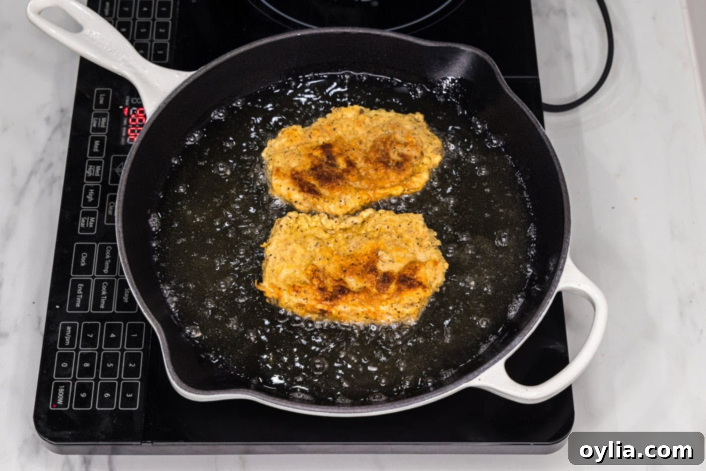 Perfectly fried chicken burgers resting in a skillet with the remaining hot oil, ready to be removed.