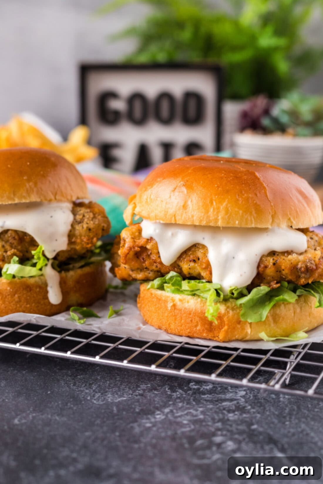 Two freshly cooked Crispy Chicken Burgers resting on a parchment-lined wire rack, showcasing their perfectly golden and crunchy coating.