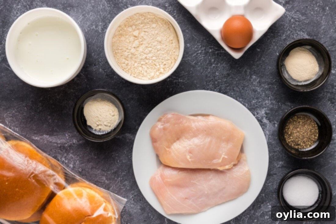 A flat lay of ingredients for making Crispy Chicken Burgers, including chicken breasts, flour, spices, buttermilk, eggs, and buns.