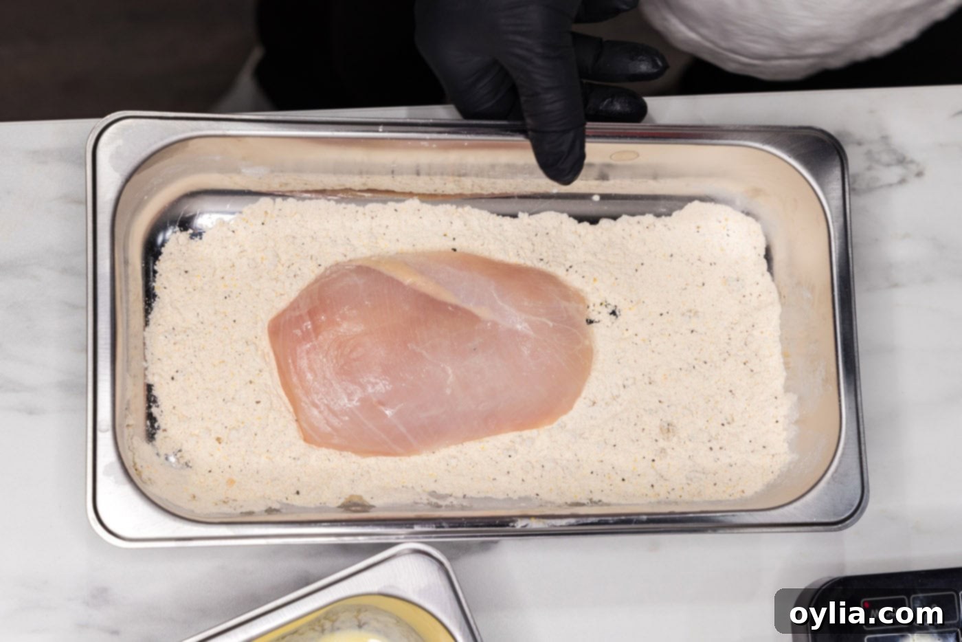 A chicken breast, fully coated in the seasoned flour mixture, being gently pressed to ensure adhesion.