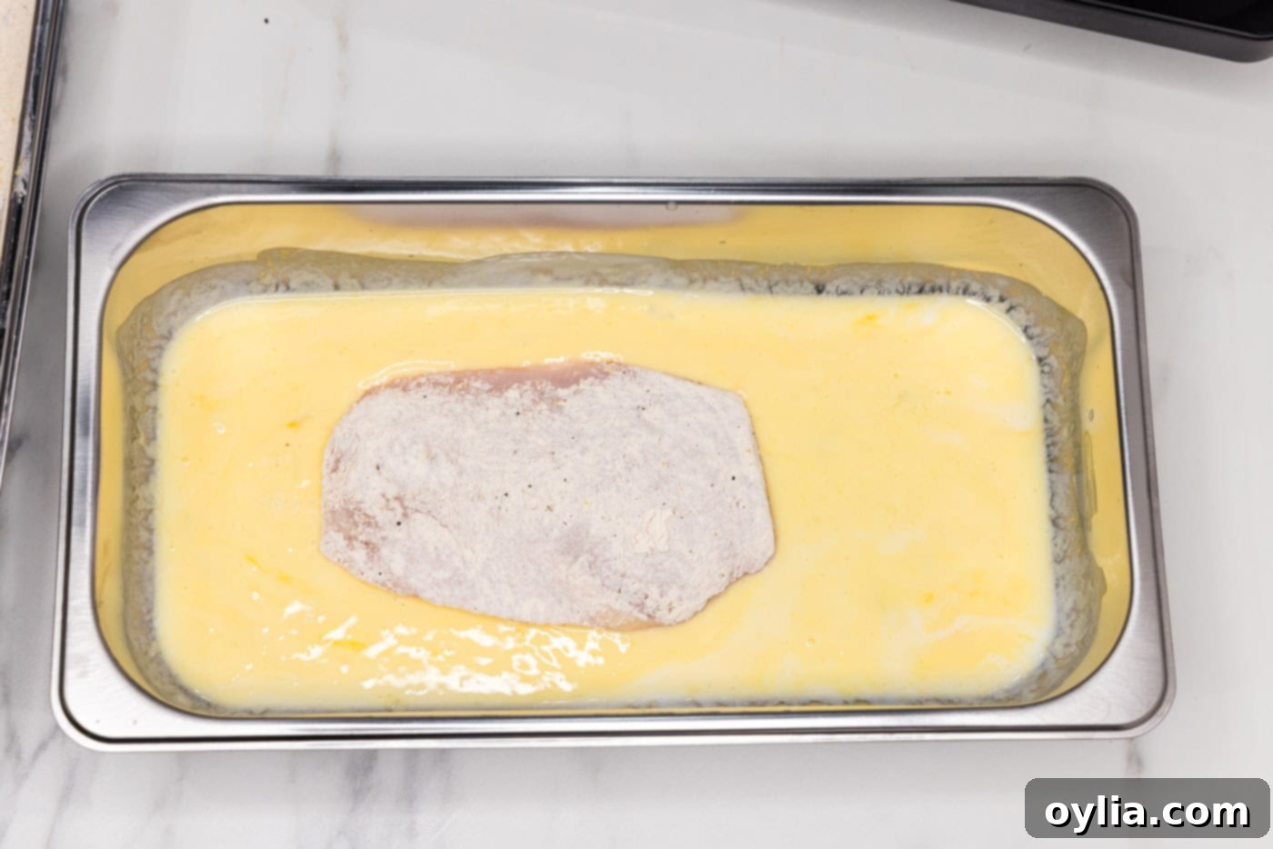 A breaded chicken breast being dipped and coated in the creamy buttermilk mixture.