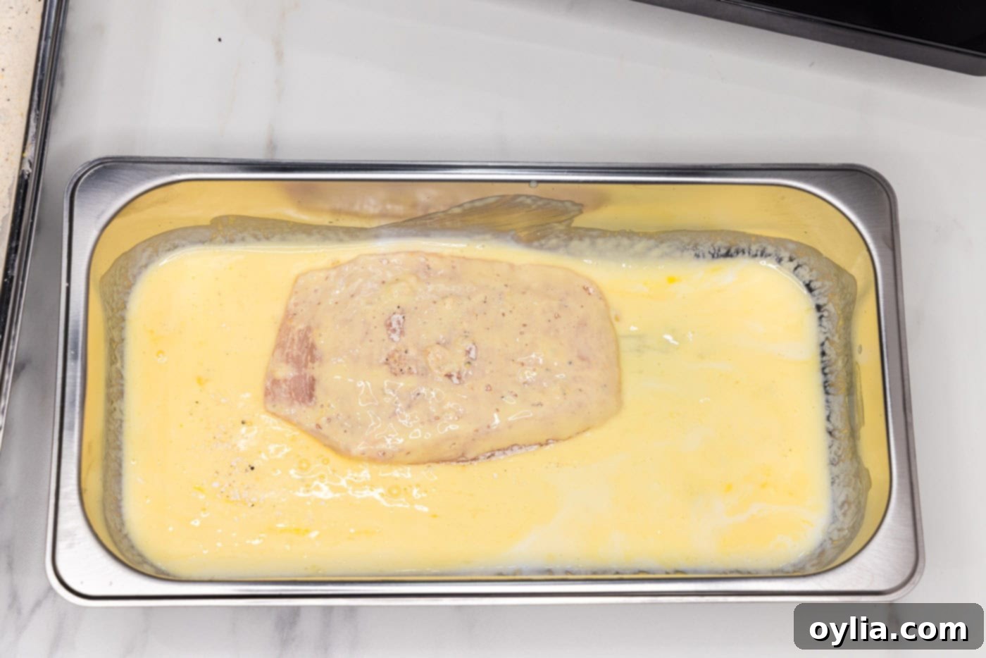 A close-up of a fully dredged chicken breast soaking in the buttermilk and egg mixture.