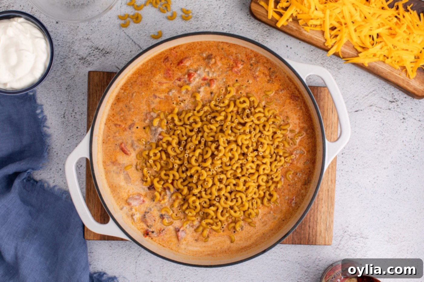 adding noodles to taco macaroni and cheese in a skillet