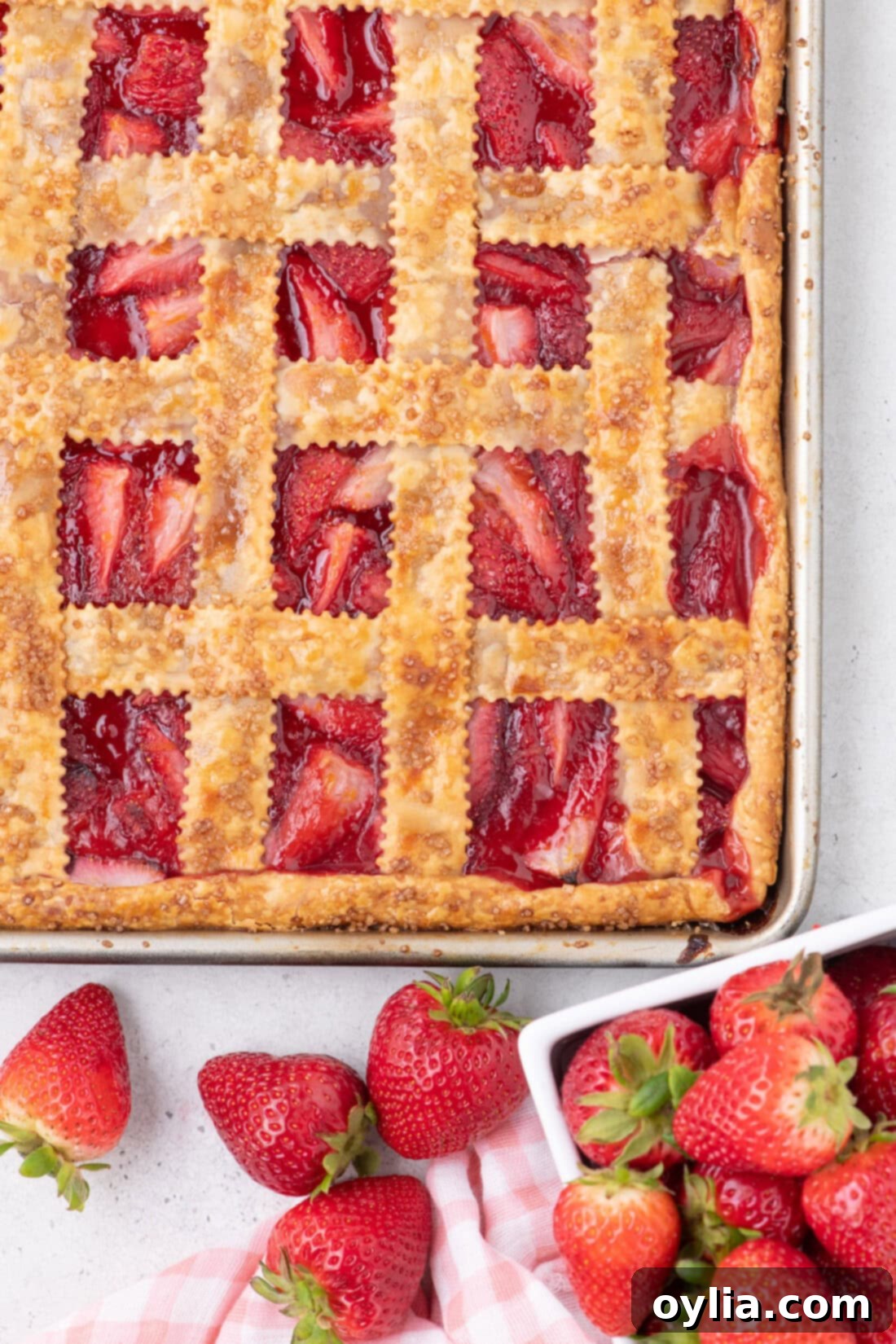 Overhead photo of a glistening Strawberry Slab Pie with a golden lattice top, showcasing the vibrant red strawberry filling peeking through.