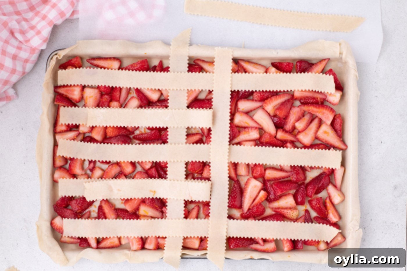 Continuing the process of weaving pie crust into a lattice top over strawberries.