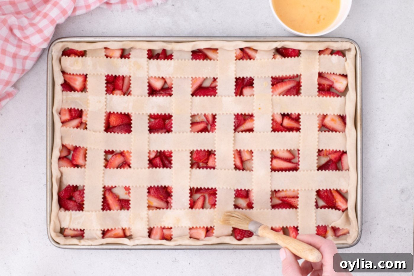 Brushing the strawberry slab pie with egg wash and sprinkling turbinado sugar over the lattice top.