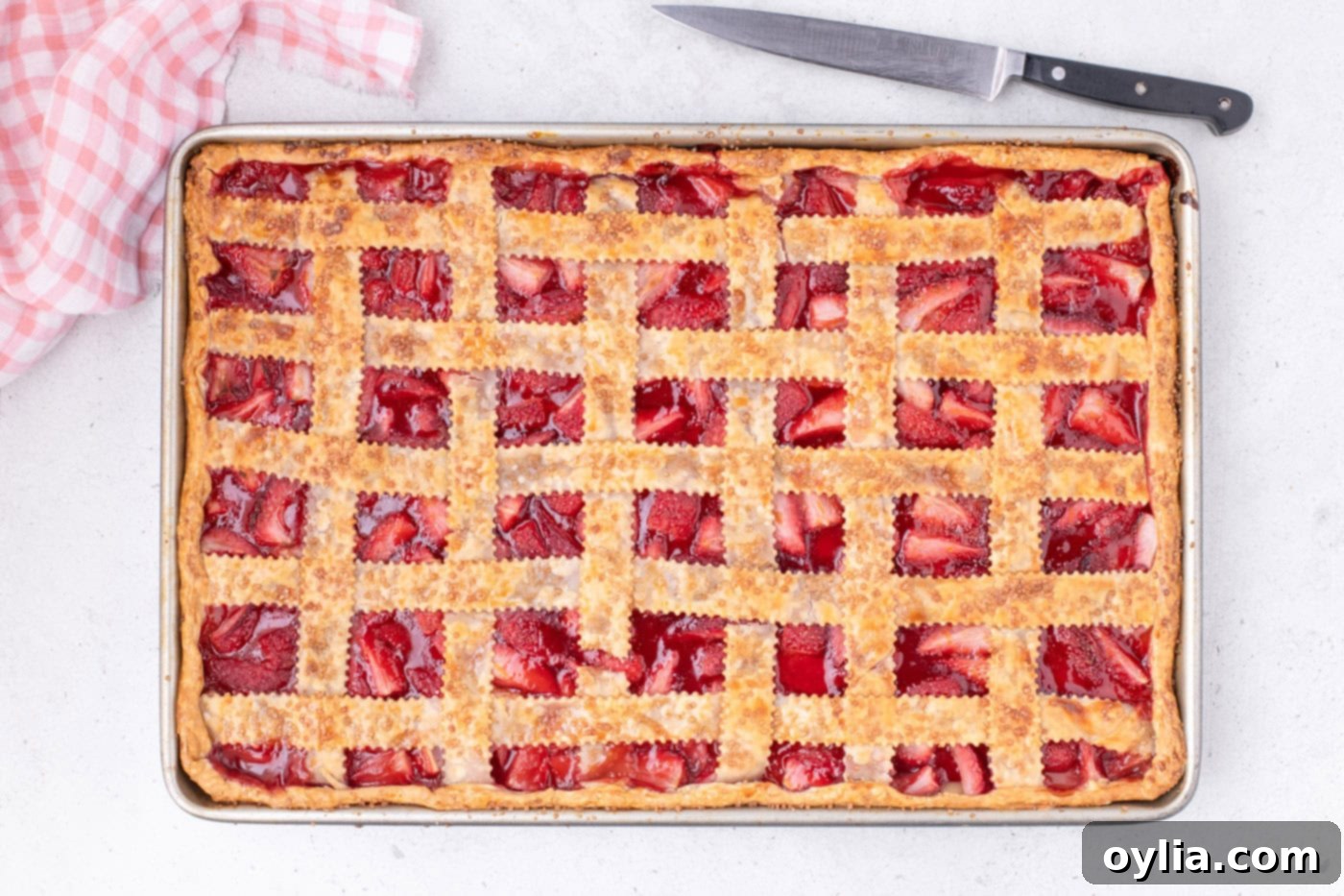 Baked overhead view of the golden-brown strawberry slab pie, with the filling bubbling through the lattice.