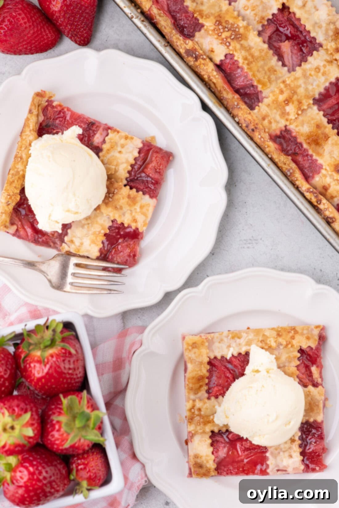 Two generous slices of Strawberry Slab Pie on white plates, each topped with a scoop of creamy vanilla ice cream.