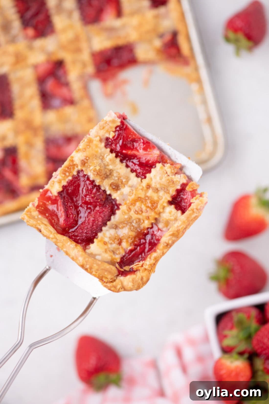 A spatula holding up a perfect slice of Strawberry Slab Pie, showing the layers of flaky crust and juicy strawberry filling.