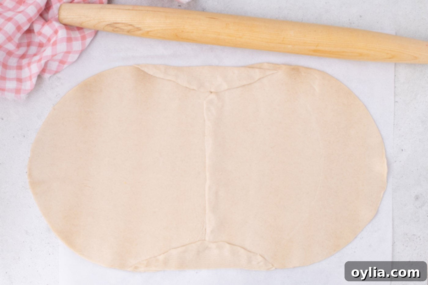 Joining two pie crusts together with a rolling pin to form a larger rectangular base for the slab pie.
