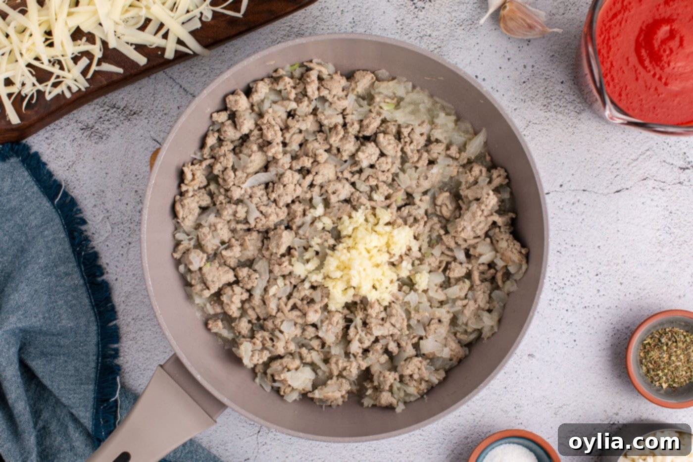 Cooked ground turkey and onion mixture in a skillet with garlic just added, releasing its fragrance.
